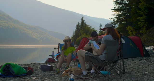 Three friends are seated on foldable chairs by a mountain lake during summer. Two tents are set up nearby. They are surrounded by nature with mountains, trees, and the calm waters of the lake. This is ideas for depicting outdoor adventures, camping trips, and vacations in nature. Perfect for promoting outdoor gear, travel and leisure activities, and nature retreats.