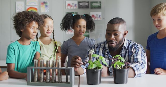 This image shows a teacher in a classroom setting, demonstrating plant growth to an interested and diverse group of schoolchildren. The students are engaging attentively, showing curiosity and interest in the science experiment. This visual is ideal for use in educational content, e-learning materials, promotional materials for science programs, and diversity in education campaigns.