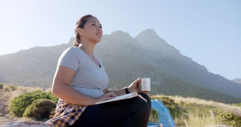 Woman Journaling in Mountainous Landscape While Drinking Coffee