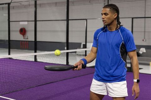 African american athlete playing padel holding racket and bouncing ball on purple court
