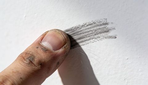 Closeup dirty thumb smudging graphite pencil marks on textured white painted wall