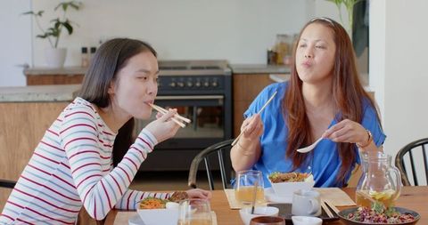 Asian Family Enjoying Meal at Dining Table in Kitchen