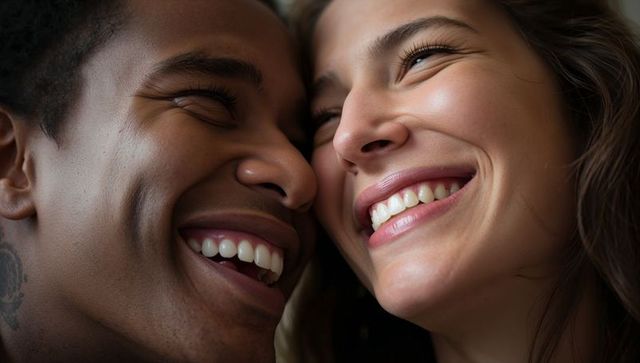 Laughing couple pressing cheeks together, sharing bright smiles, intimate joyful closeup