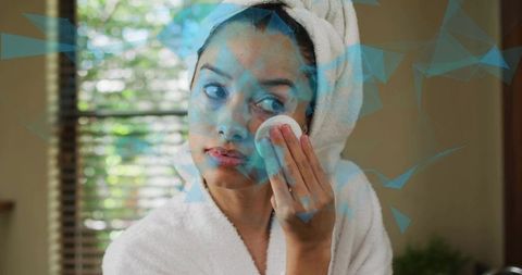 Young woman applying toner with cotton pad at bathroom vanity wearing towel turban
