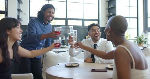 Friends toasting in modern kitchen clinking glasses during daytime celebration