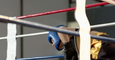 Male boxer leaning on ropes wearing blue headguard and black gloves closeup in ring