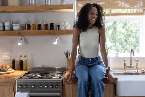 African american woman sitting on wooden countertop smiling in modern rustic kitchen