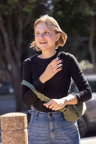 Young woman smiling on sunny urban street wearing black top, denim jeans, crossbody bag