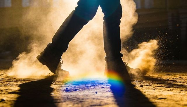 Backlit boots kicking dust with sunbeam rainbow, dramatic shadows and dust particles