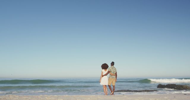 Back view of diverse couple hugging on beach and looking on sea. Summer, relaxation, happy time, romance.