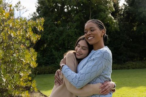 Smiling friends hugging in garden, casual knit sweaters, outdoor warmth and connection