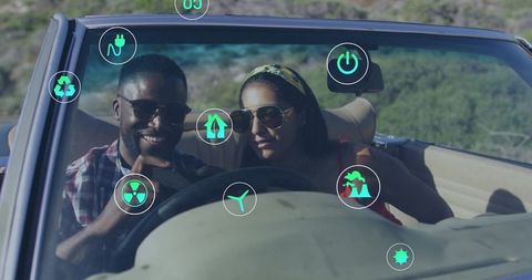 Couple driving convertible with ar eco icons on windshield along scenic road
