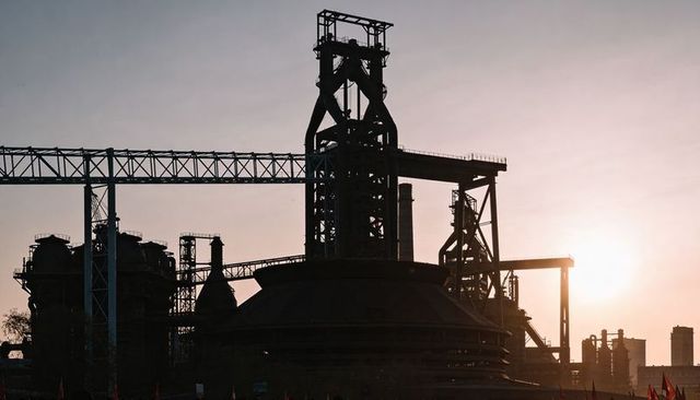 Blast furnace tower dominating steelworks silhouette at sunset with conveyor bridge
