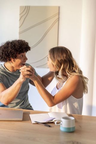 Sunlit couple sharing joyful moment holding hands at kitchen table, casual home lifestyle