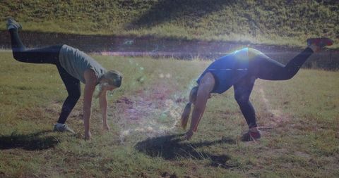 Partner balancing single-leg lifts in sunlit meadow for outdoor fitness and coordination