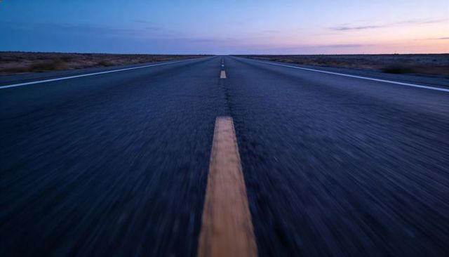 Low-angle twilight highway vanishing into horizon with golden centerline and motion blur