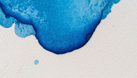 Cobalt turquoise watercolor pool forming granular wash on textured off-white paper closeup