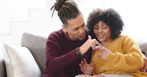 Couple sharing intimate engagement moment on sofa with man placing ring
