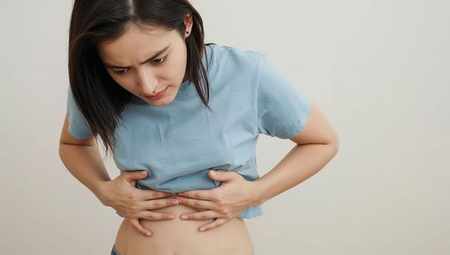 Asian woman clutching lower abdomen, showing abdominal pain, wearing cropped tee and jeans