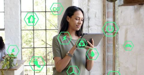 Woman using tablet monitoring green energy icons in modern loft coworking space