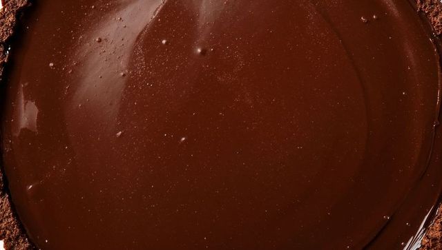 Glossy dark chocolate ganache tart closeup with crumbly cocoa crust, studio macro food