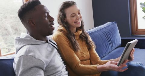 Diverse Couple Enjoying Leisure Time with Tablet on Couch