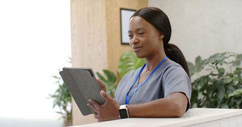 African nurse at clinic reception holding tablet and smiling, modern healthcare staff