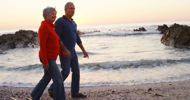 Happy senior caucasian couple holding hands and walking on beach by sea at sunset. Retirement, relationship, love, togetherness, free time and relaxing, unaltered.