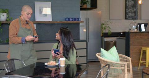 Barista taking mobile order while indian customer browsing phone and enjoying coffee