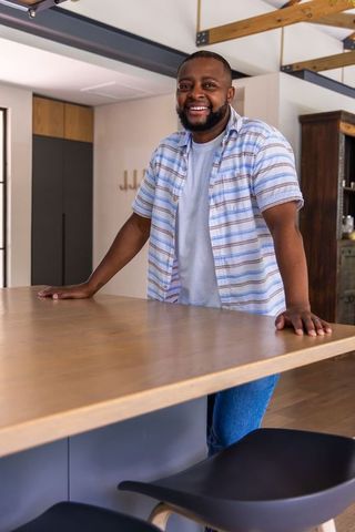 Smiling man leaning on wooden kitchen island in modern open-plan kitchen with exposed beams