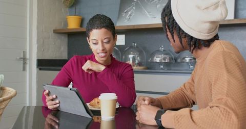 Diverse young adults sharing tablet and coffee while discussing ideas in cozy modern cafe