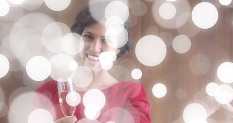 Smiling woman in red dress toasting with champagne amid soft bokeh lights for celebration