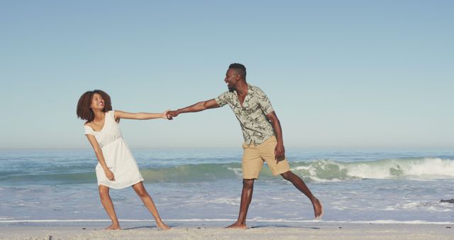 Happy diverse couple holding hands and laughing, having fun on sunny beach by the sea. Summer, free time, relaxation, romance and vacations.