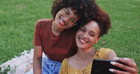 African American friends smiling and taking selfie on pink blanket in sunlit park