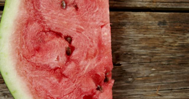 A close-up view of a juicy slice of watermelon on a rustic wooden surface, with copy space. Its vibrant red flesh and scattered black seeds make for a refreshing summer treat.
