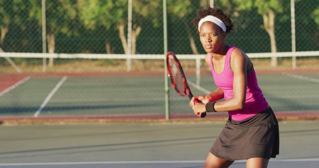 Depicts focused female tennis player ready to return a shot on an outdoor court. Suitable for use in stories about sports, fitness, determination, and women's athletics. Ideal for articles on athletic training, advertisements for sportswear, and motivational posters.