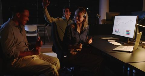 Diverse team analyzing data on computer in modern office at night