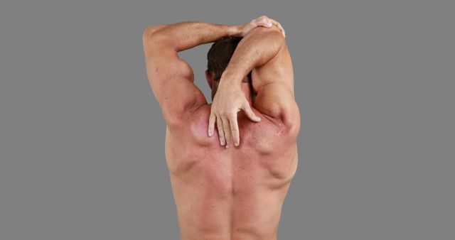 This image shows a man stretching his back muscles with his arm extending over his shoulder against a gray background. It can be used for fitness and wellness blogs, exercise guides, workout routines, and health-related articles.