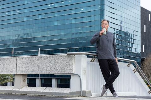 Mature man pausing for hydration on urban overpass with glass skyscraper backdrop