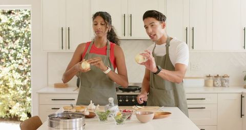 Diverse couple peeling onions and prepping fresh ingredients on sunlit kitchen island