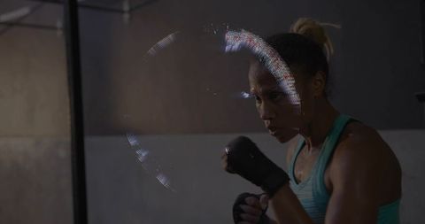Woman boxer training hardcore in gritty gym wearing teal tank and black hand wraps