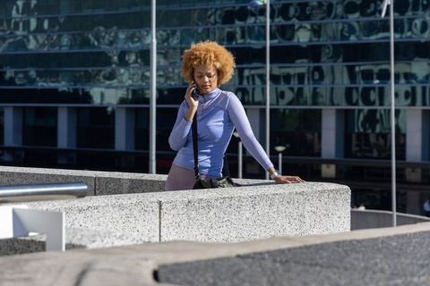 African american woman talking on phone, leaning on concrete ledge by glass office facade