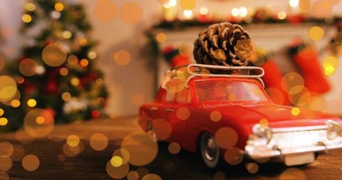 Vintage red toy car carrying pinecone on roof rack with christmas bokeh lights