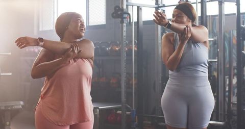 Diverse women stretching shoulders and chatting in gym during group workout session