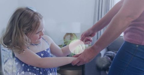 Young daughter reaching and holding mother's wrist, playful bonding in family living room