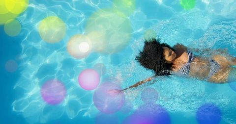 Woman floating on back in turquoise pool with sunlit caustics and dreamy bokeh