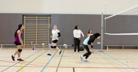 Multicultural women playing indoor volleyball, team training and teammate coordination