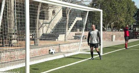 Goalkeeper reacts to approaching soccer ball in outdoor field