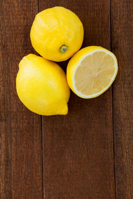 Close-up of whole and half lemons on wooden table. Ideal for use in food blogs, recipe websites, health and wellness articles, or kitchen decor inspiration.