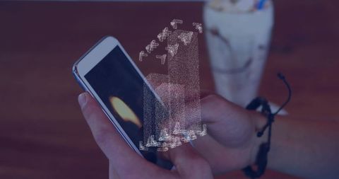 Hands holding smartphone projecting holographic flame and data particles over wooden table